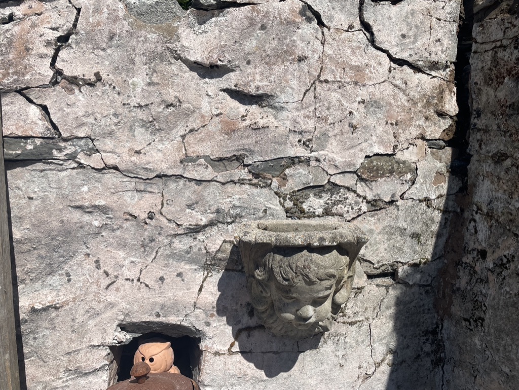 Cracked wall surface with a small stone face planter below it.