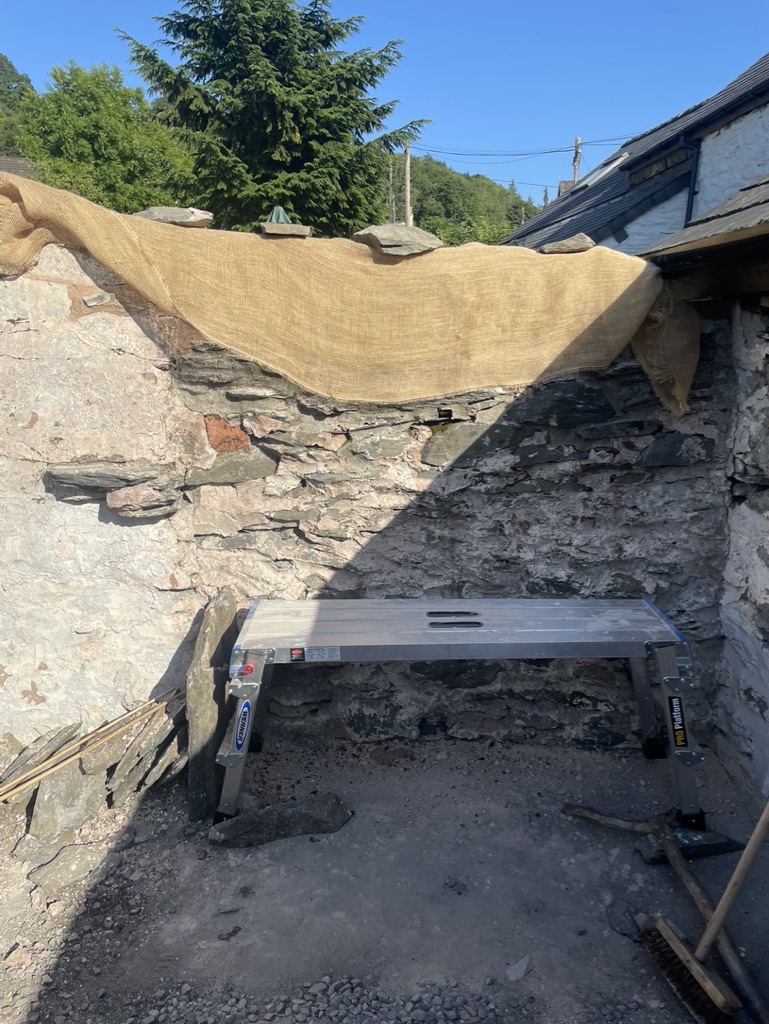 Old slated garden wall under hessian with a work platform below.