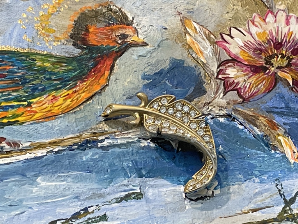 Discarded gold jewellery placed into a colourful mixed-media artwork with a painted bird and flower.