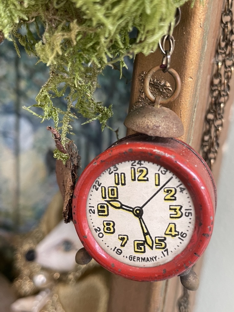 Close-up of a small red clock hanging among moss and miniature assemblage details.