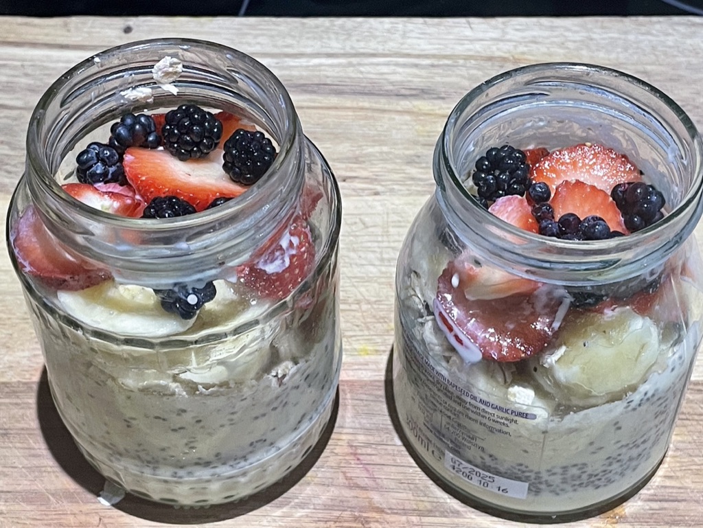 Two jars of overnight oats topped with strawberries, blackberries, blueberries and banana.