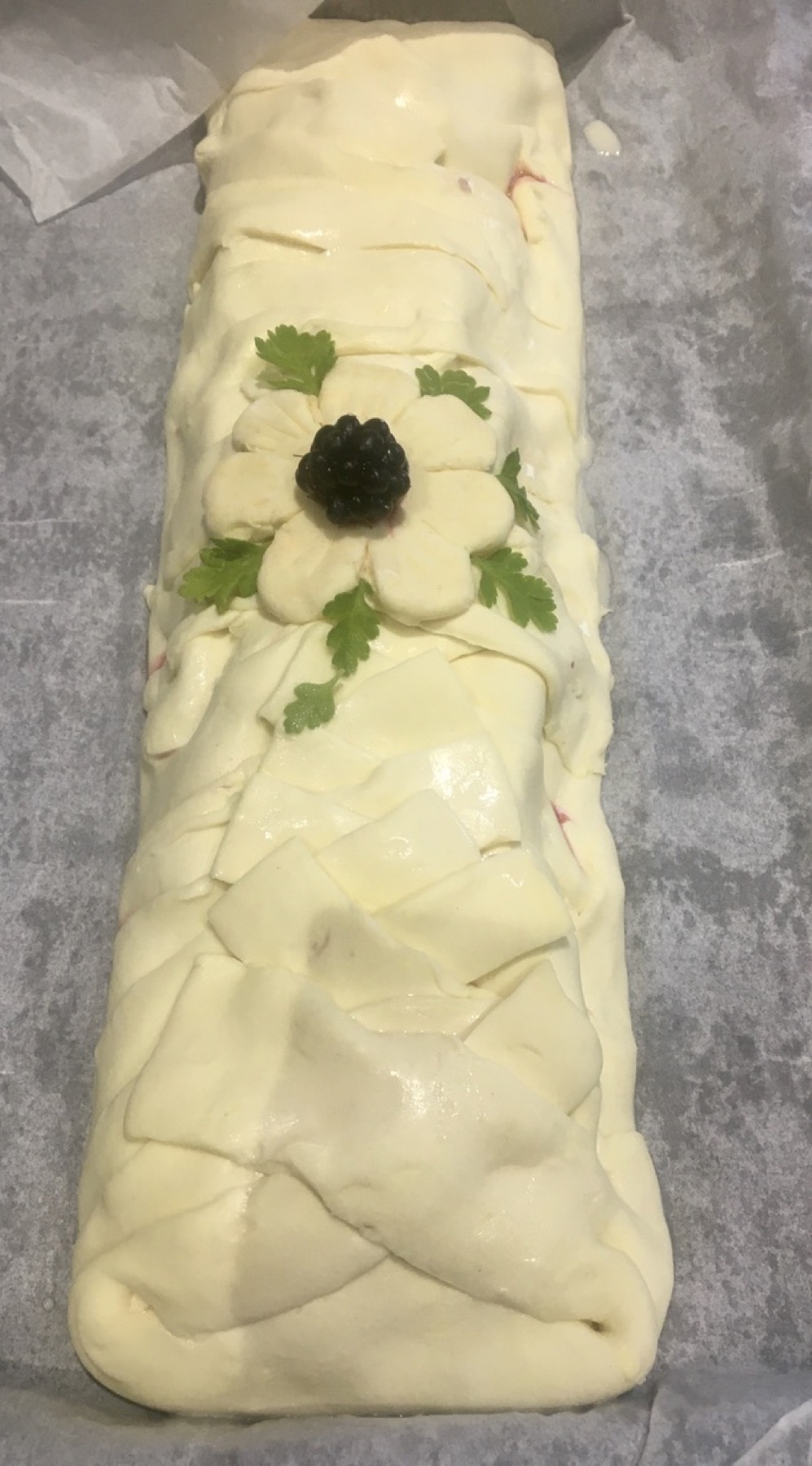 Unbaked apple and blackberry strudel decorated with pastry flowers and a blackberry.