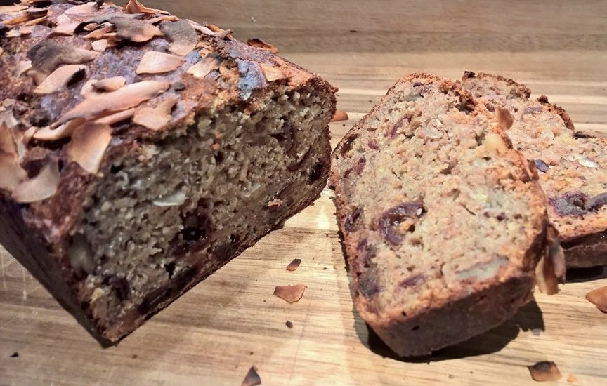 Auntie Dot's banana and Medjool date loaf sliced on a wooden board with toasted almond flakes.