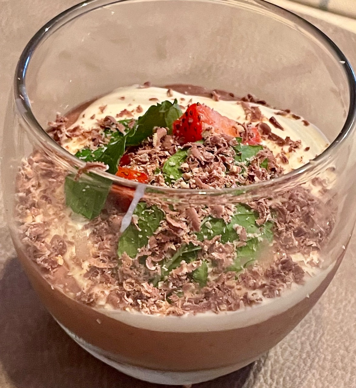 Chia seed and cacao chocolate mousse in a glass topped with cream, raspberry, fresh mint and grated chocolate.