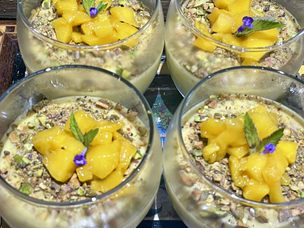 Four glasses of mango and coconut chia mousse topped with crushed pistachios, mango and mint.