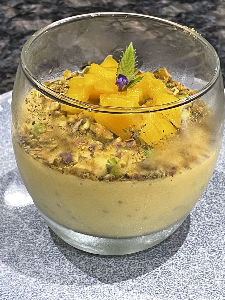 Mango and coconut chia mousse topped with crushed pistachios, mango, mint and a small edible flower.