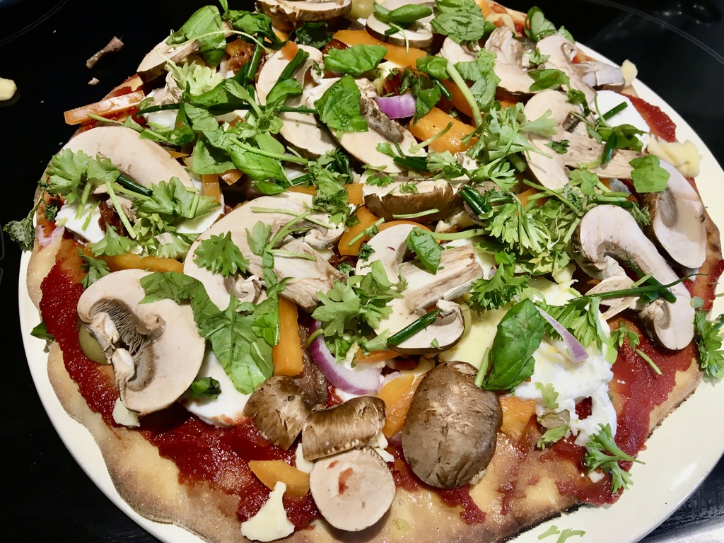 Homemade pizza topped with mushroom, red onion, kale, herbs, tomato puree and vegan cheese.