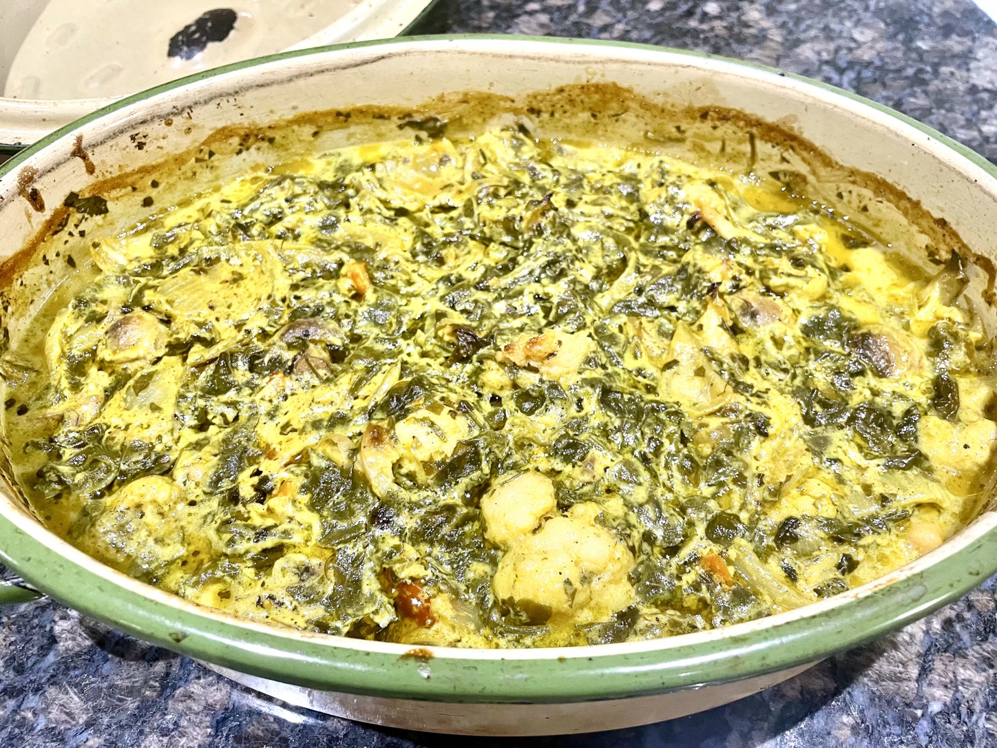 Creamy coconut mushroom curry with greens in a green casserole dish.