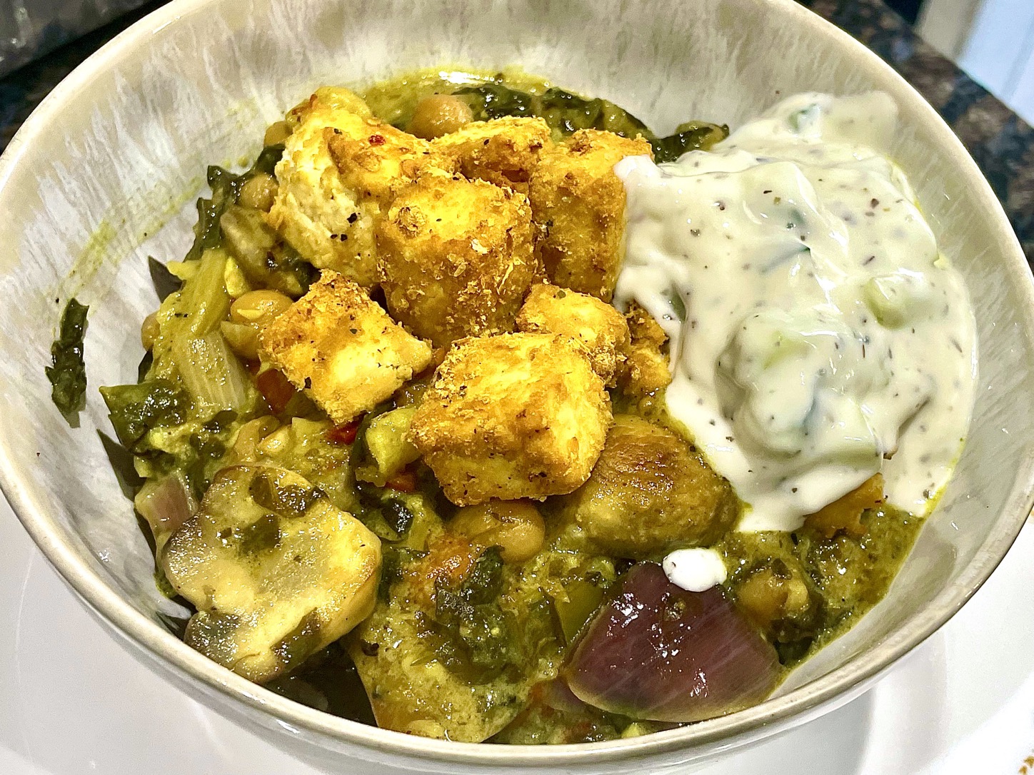Creamy coconut mushroom curry served in a bowl with crispy tofu and cucumber yoghurt.