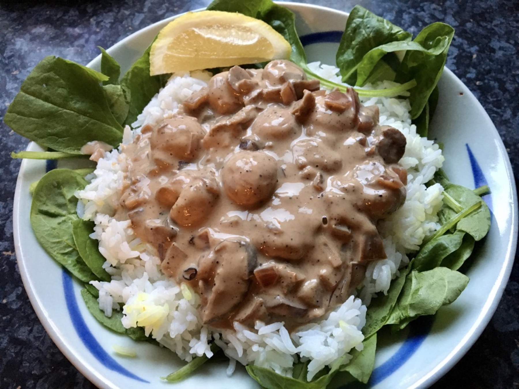 Mushroom strogonoff served over rice with spinach leaves and a lemon wedge.