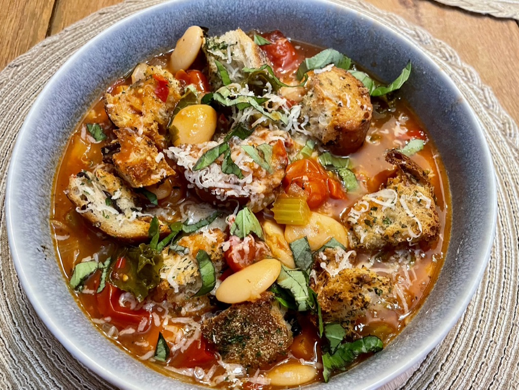 Rustic Tuscan ribollita with butterbeans, tomatoes, herbs, grated vegan cheese and toasted bread pieces.