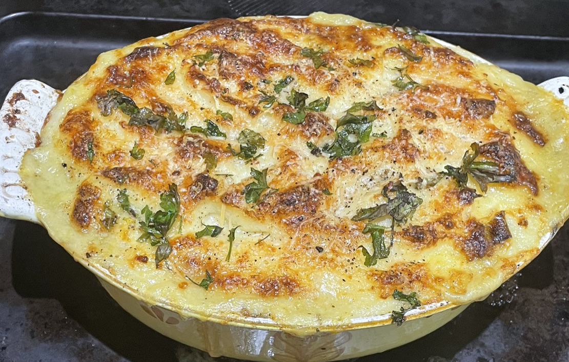 Golden baked vegan Shepherdess Pie with an oozing topping and herbs in a casserole dish.