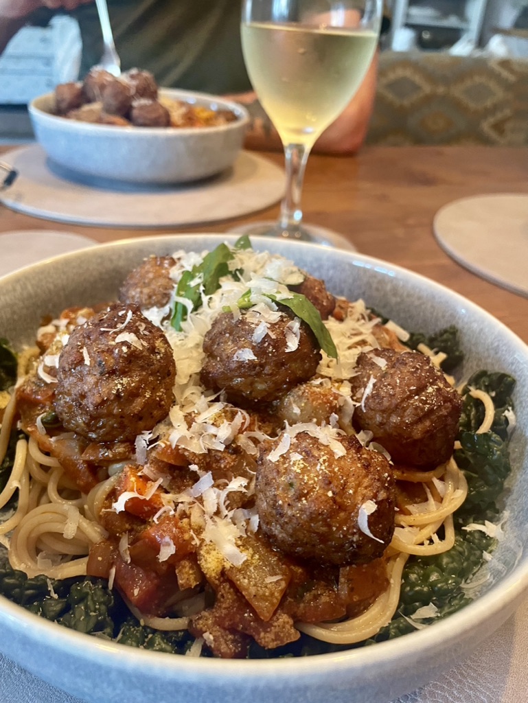 Vegan meatballs and spaghetti served at the table with a glass of white wine.