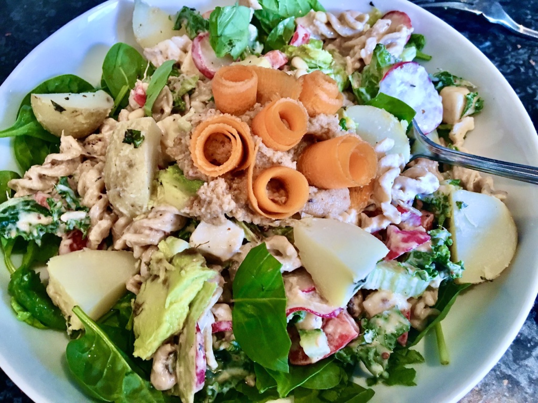 Buddha Bowl with pasta, potatoes, greens, radishes, carrot ribbons, avocado and hummus.
