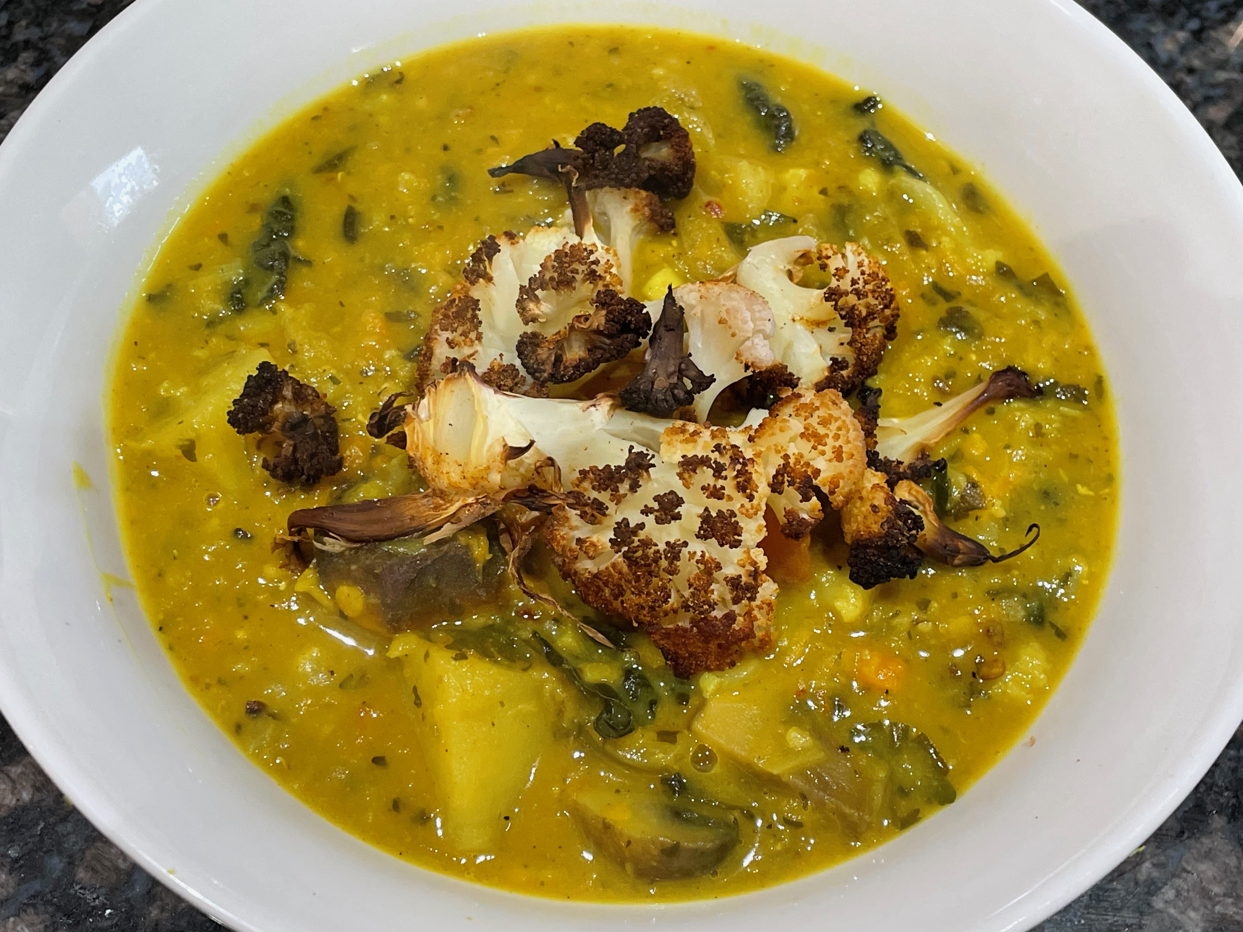 Roasted cauliflower curried broth in a white bowl with lemon, coriander and roasted cauliflower florets.